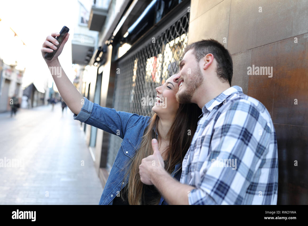 Happy couple taking selfies with smart phone standing in the street Stock Photo