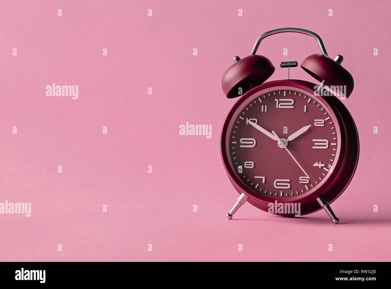 Old fashioned red alarm clock with bells centered over a pink