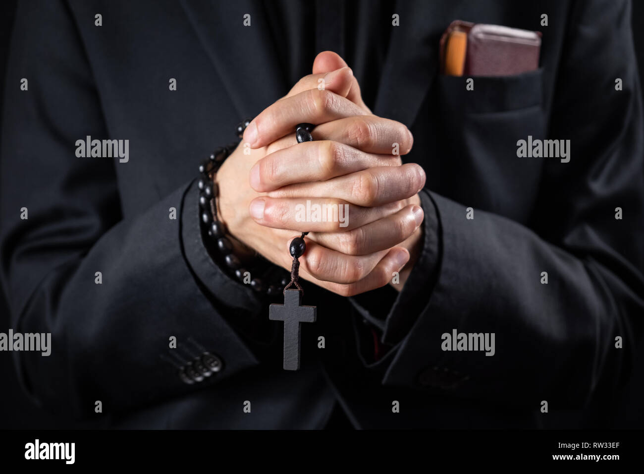 Christian person praying, low key image. Hands of a man in black suit or a priest portraying a preach Stock Photo