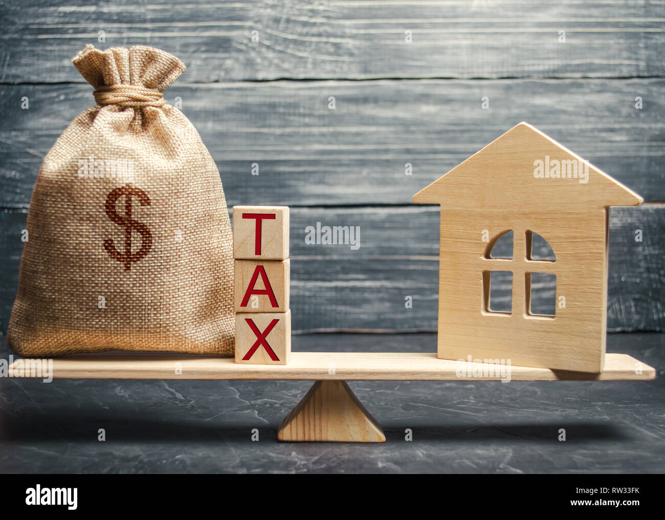 Wooden house and a money bag with the word Tax on the scales. Taxes on real estate, payment