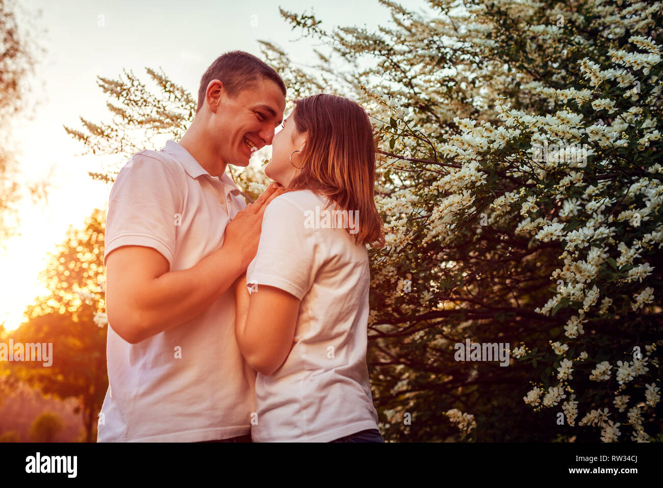 Happy couple walking in spring blooming park at sunset. Young man and woman holding hands and smiling Stock Photo