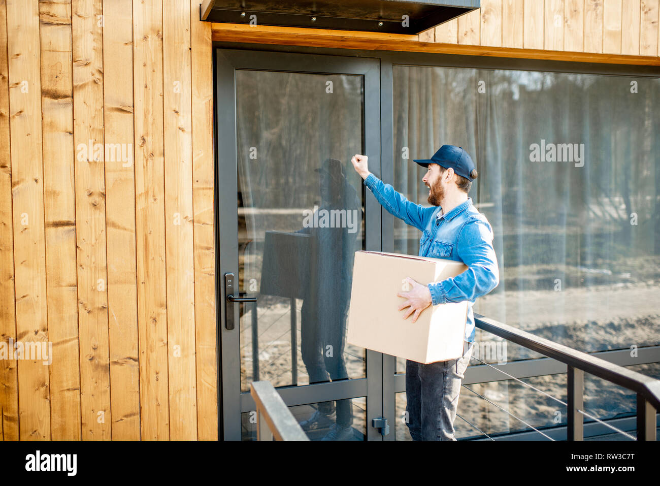Delivery man knocking door of the modern house, delivering some goods ...