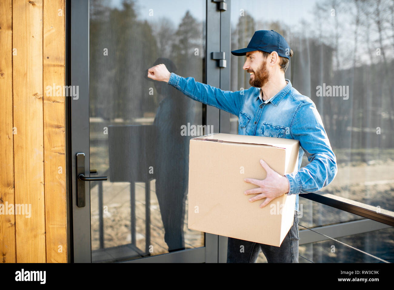 Delivery man knocking door of the modern house, delivering some goods in the paper parcel home Stock Photo