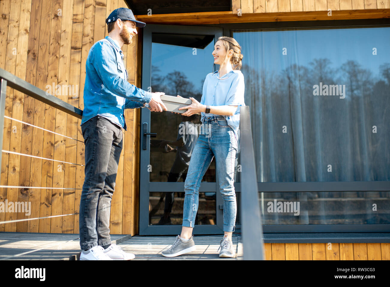 Delivery man bringing shoes home to a young woman client. Buying clothes online and delivery concept Stock Photo