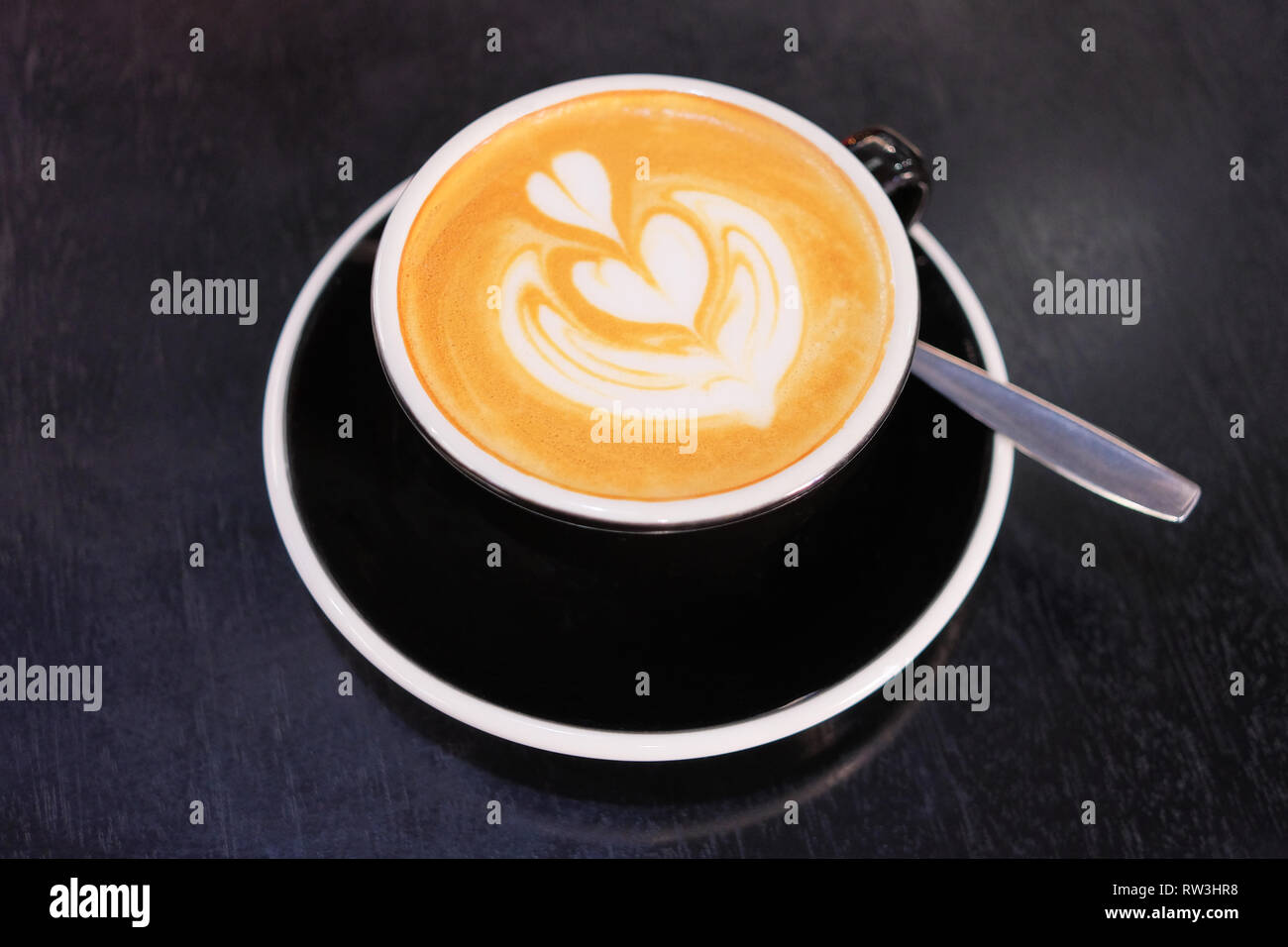 Black coffee cup with heart shape latte art on modern dark grey table