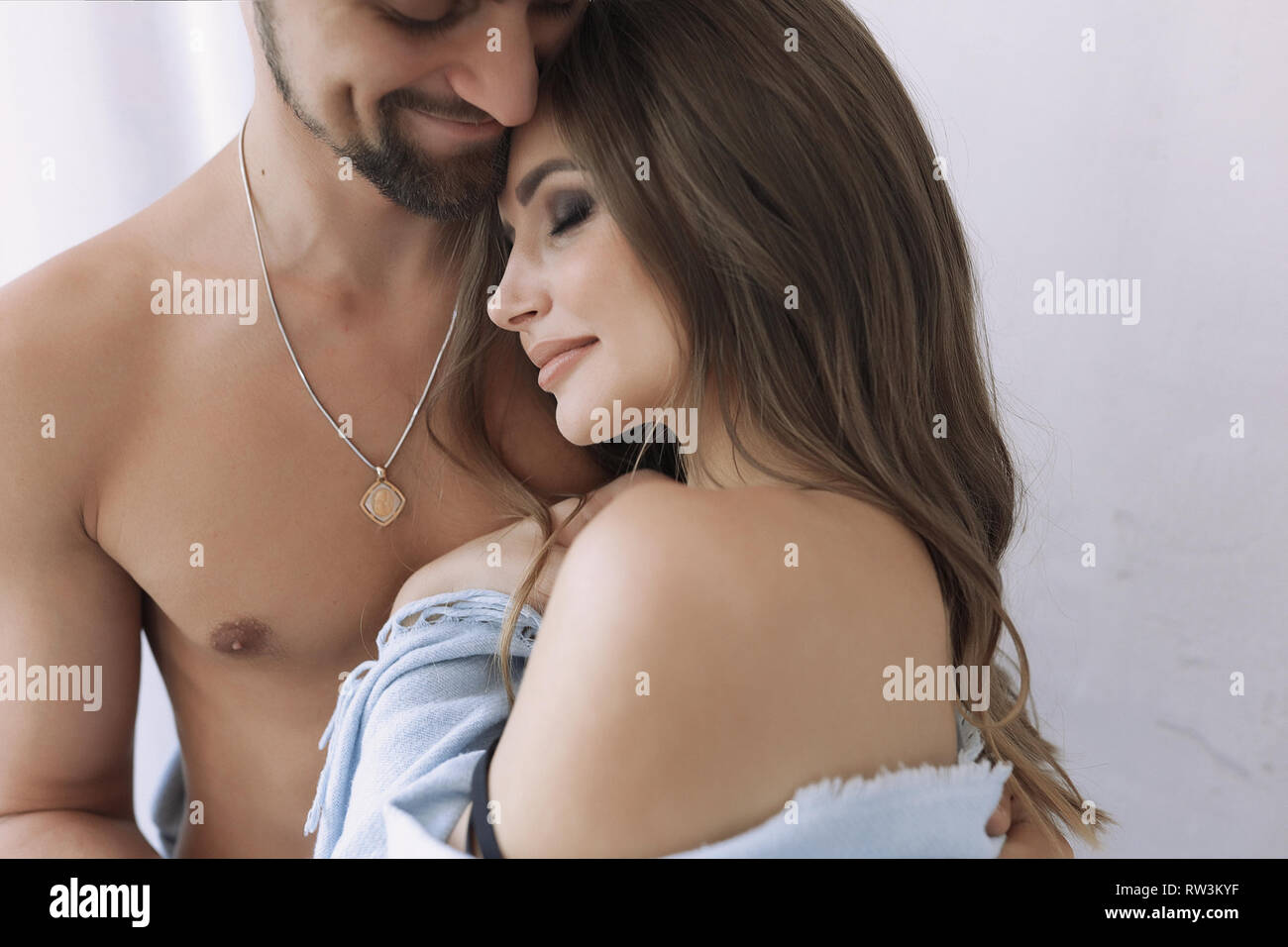 Tender happy couple hugging. Beautiful woman lying on the man's chest, makeup on the face, hairstyle. Smiling guy holding his girl, his beard on head Stock Photo
