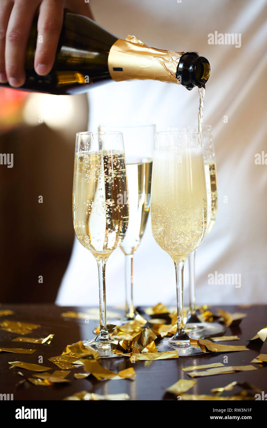 Champagne Flutes In Golden Sparkle Background with golden confetti. Man pouring sparkle wine. Close up Stock Photo