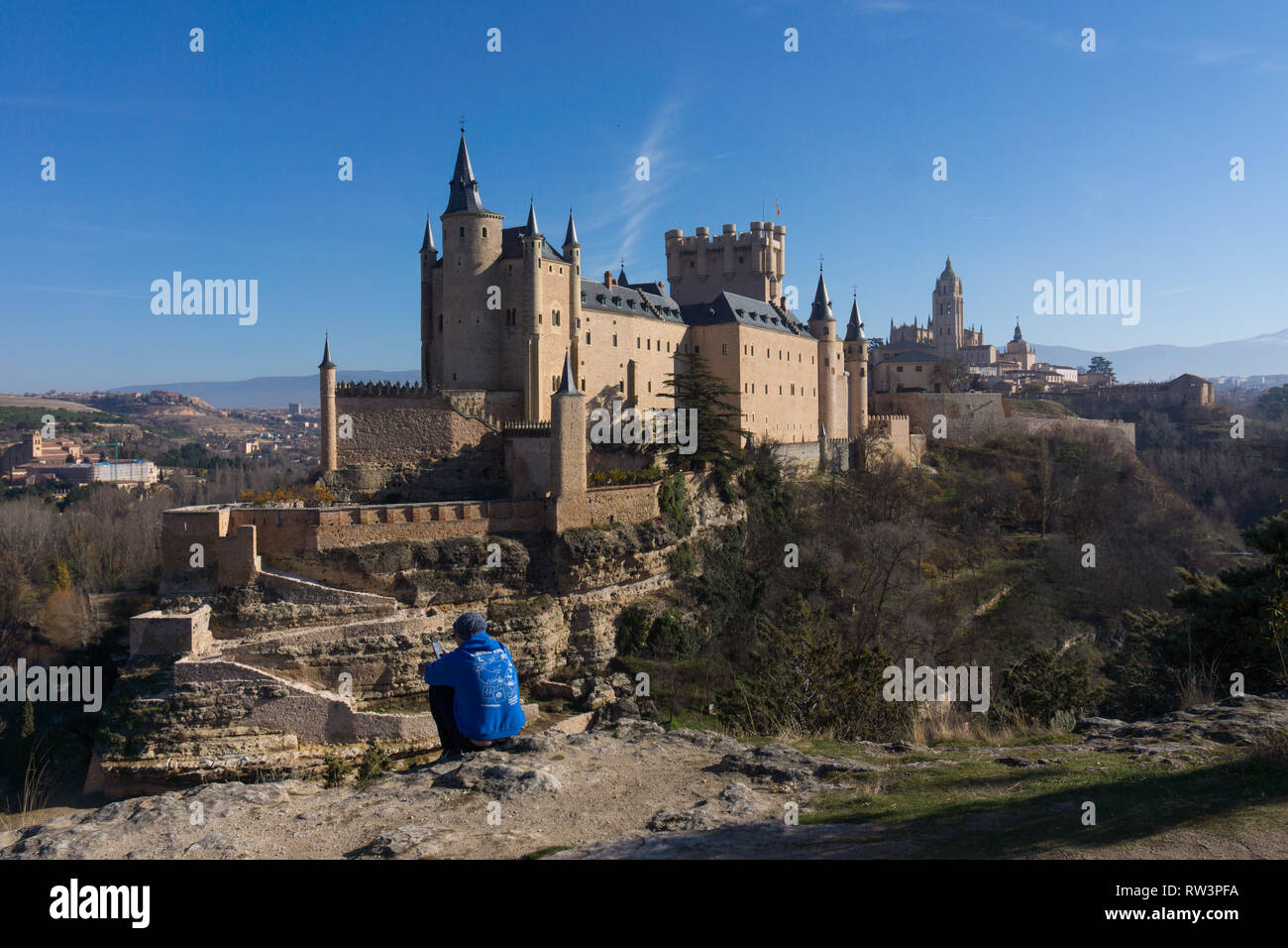 Young man sitting looking at mobile phone at viewpoint of the Alcázar de Segovia, UNESCO World Heritage Site, Segovia, Spain Stock Photo