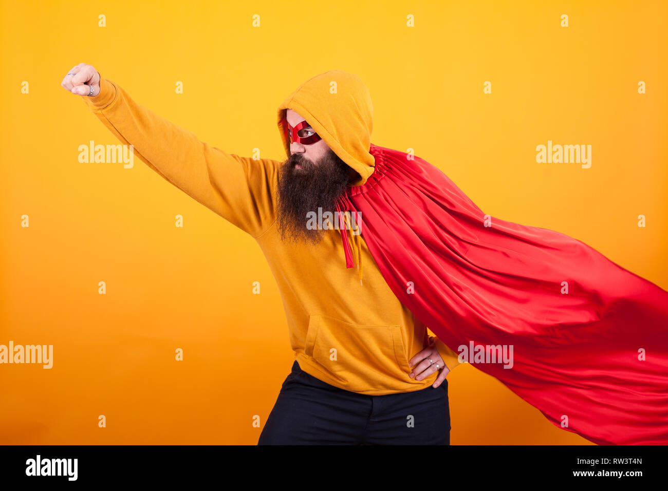 Superhero with red cape and mask flying away in studio over yellow background., Brave man. Handsome. Stock Photo