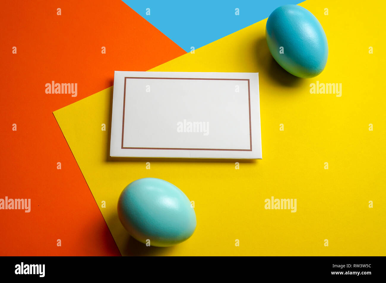 Colorful shiny easter eggs on color block background and a card with place for text Stock Photo