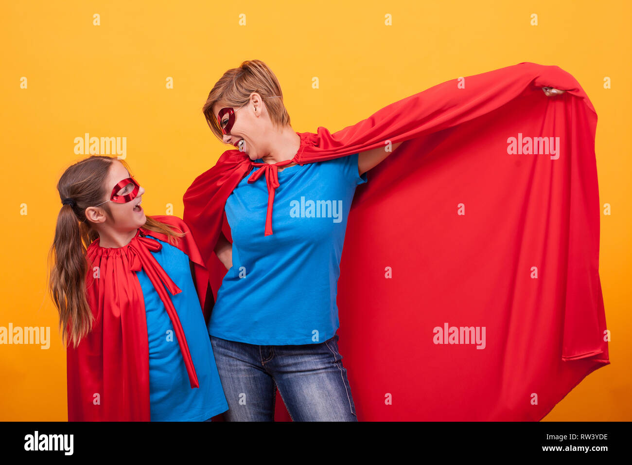 Mother and daughter dressed like superheros bonding over yellow background. Mother and daughter playing. Motherhood. Happy childhood. Stock Photo