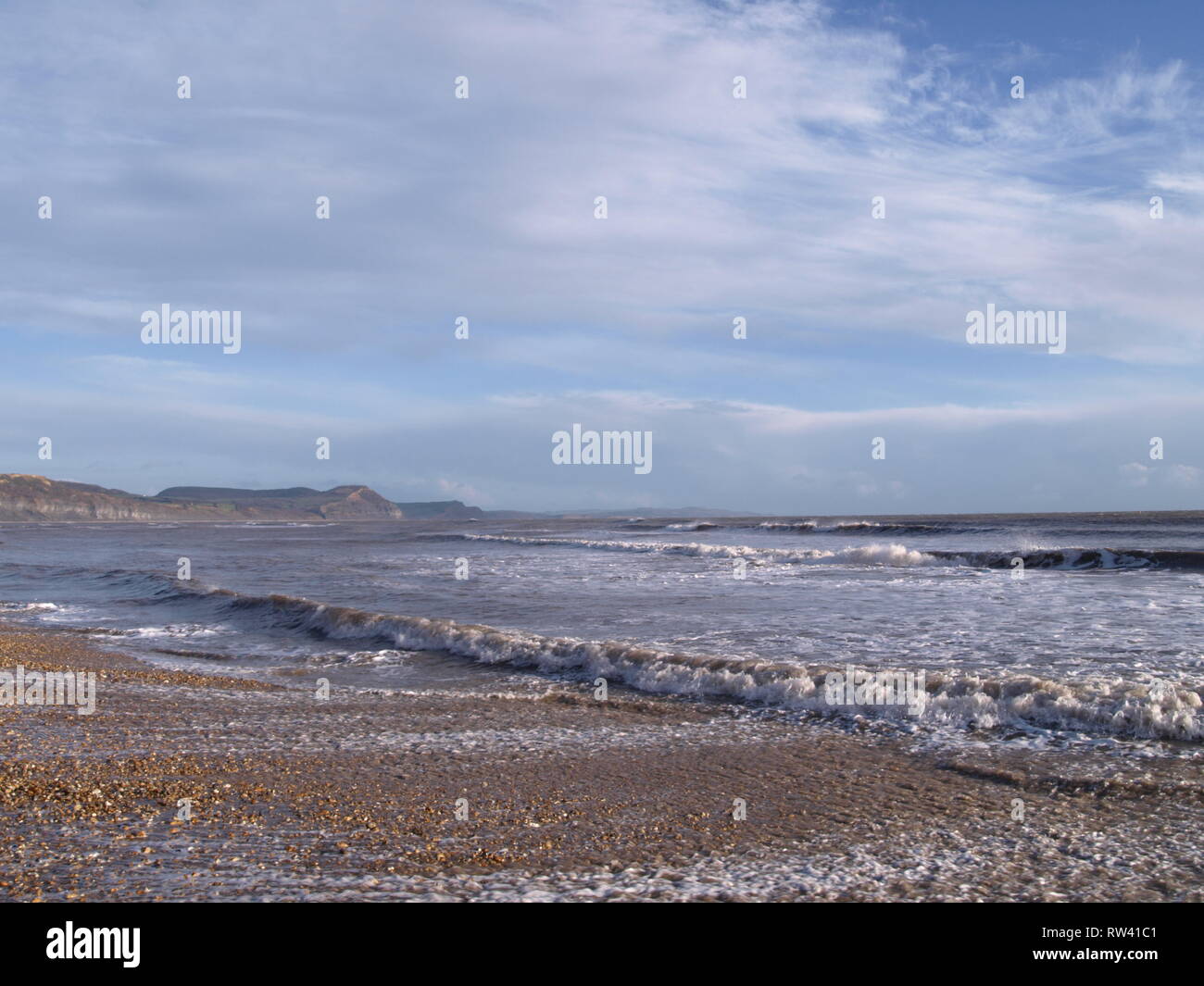 receding waves on Lyme Regis beach, dragging the shingle down the beach on a bright cold day in January Stock Photo