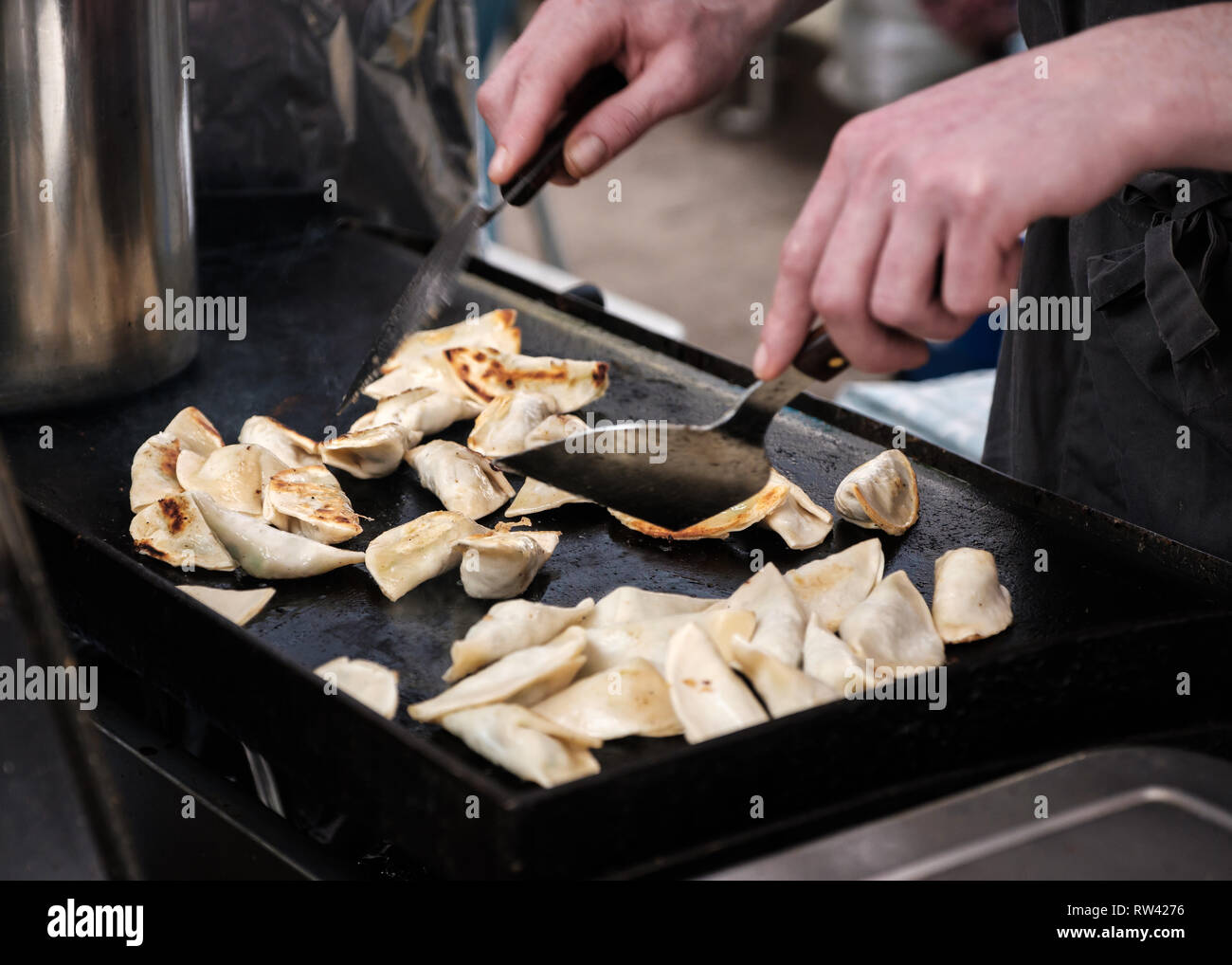 Fresh gyozas being fried and turned with spatulas on a hotplate on a street market food stall, Edinburgh, Scotland Stock Photo