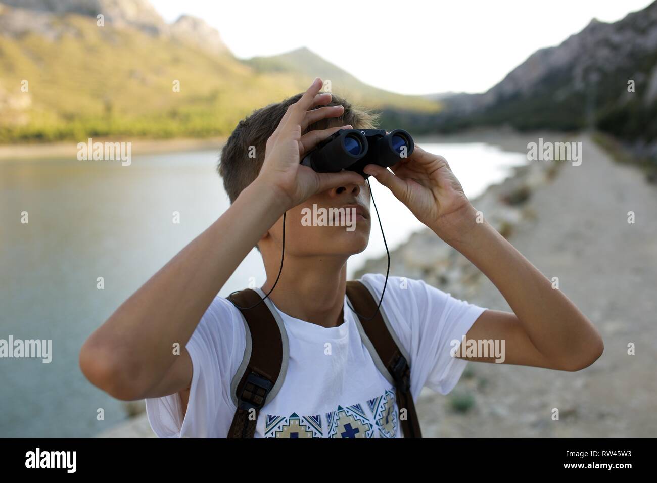 Young Boy with Binoculars spotting wildlife and birds on a beautiful river Stock Photo