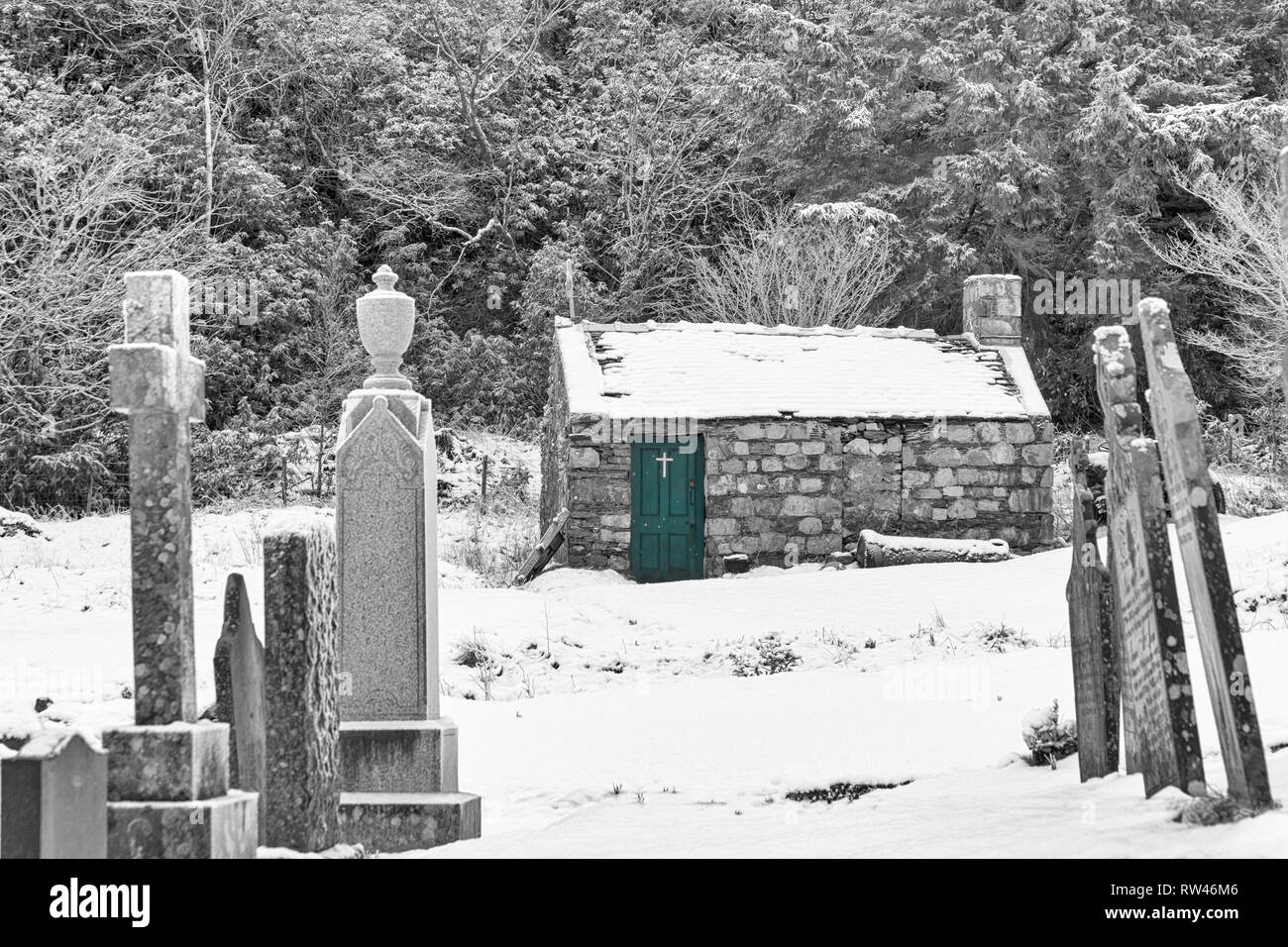 chapel in grounds of St John's Episcopal Church and gravestones in the snow at Ballachulish, Highlands, Scotland, UK on winters day in February - B&W Stock Photo
