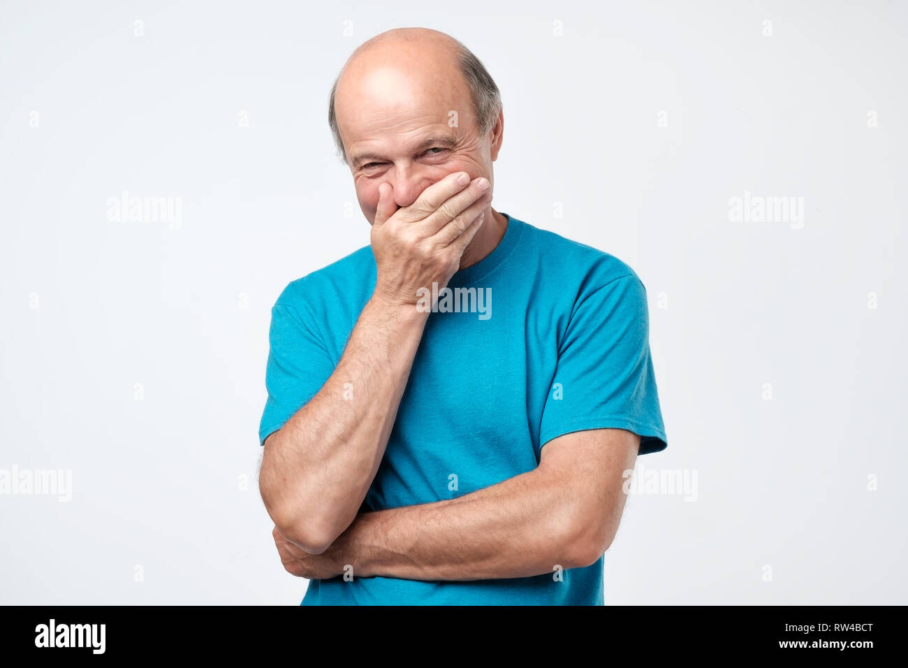Senior bald hispanic man giggles and covers mouth with his hand Stock Photo