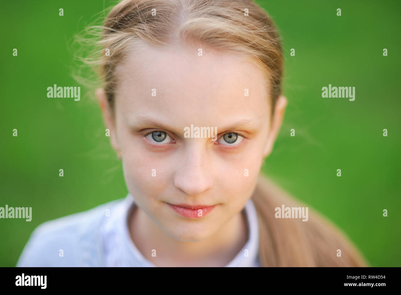 closeup portrait of beautiful blonde healthy little caucasian girl with clear skin on green outdoor spring background Stock Photo