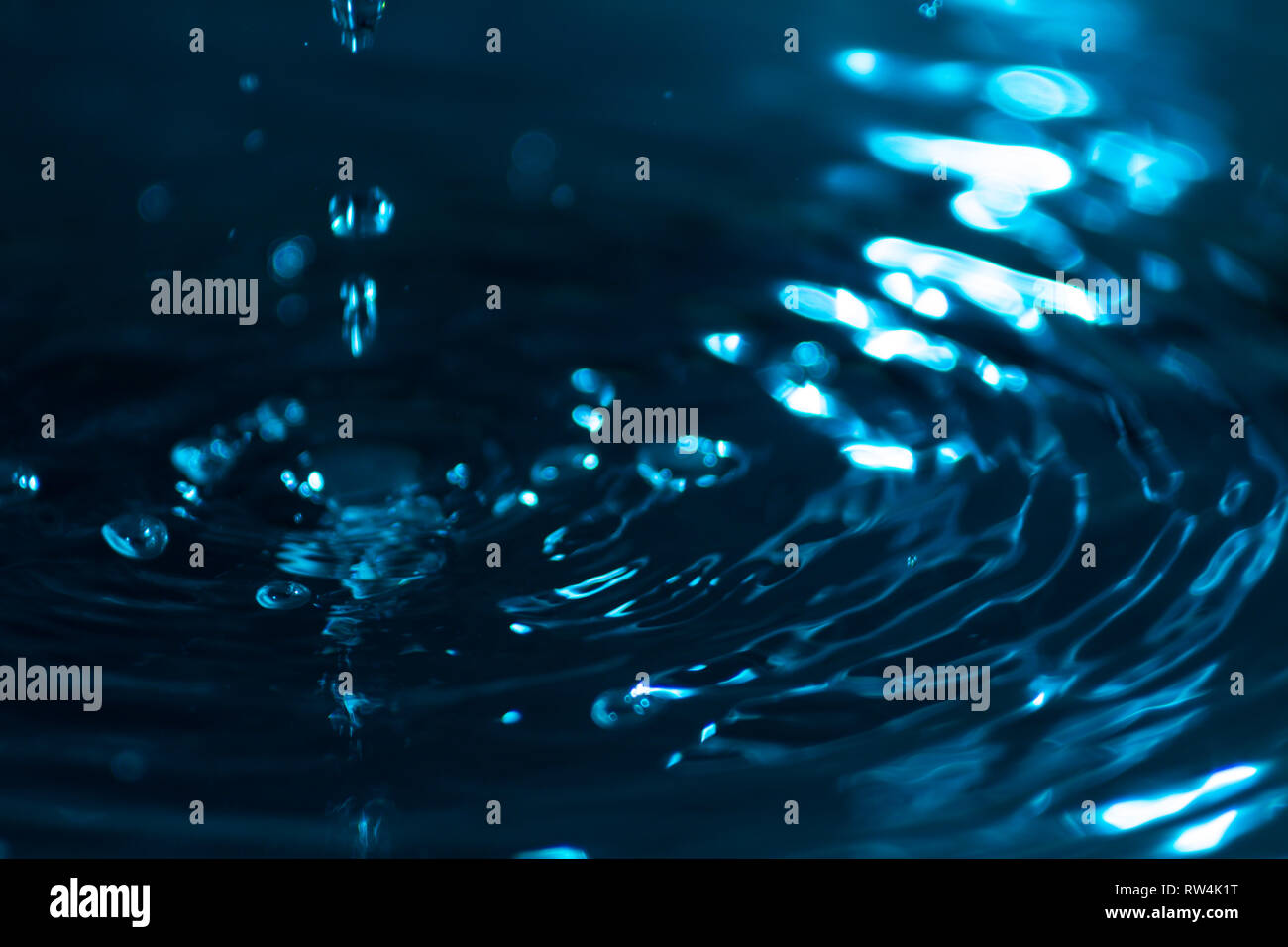 Splash of water drops on a water surface colored with celestial ink. Concept of purity, cleanliness and preservation of non-renewable resources. Abstr Stock Photo
