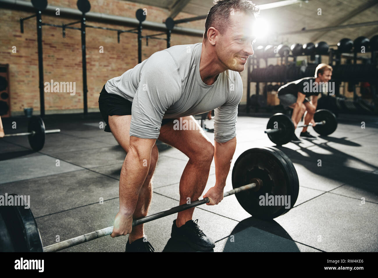Fit man in sportswear smiling while preparing to lift weights during a weight training session at the gym Stock Photo