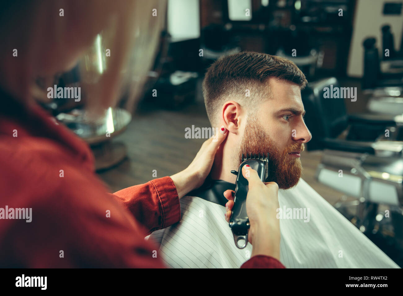 Client during beard shaving in barbershop. Female barber at salon ...