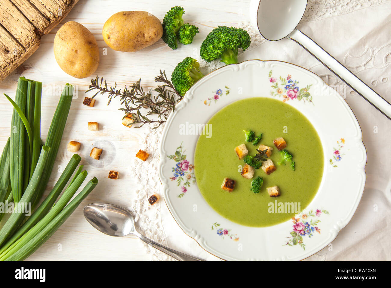 Spring detox broccoli green cream soup with potatoes and vegan cream in bowl on bright wooden board over white background, top view. Clean eating Stock Photo