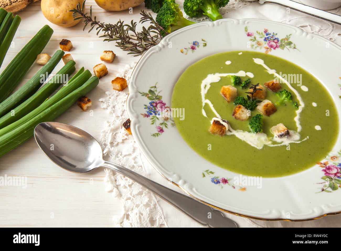 Spring detox broccoli green cream soup with potatoes and vegan cream in bowl on bright wooden board over white background, top view. Clean eating Stock Photo