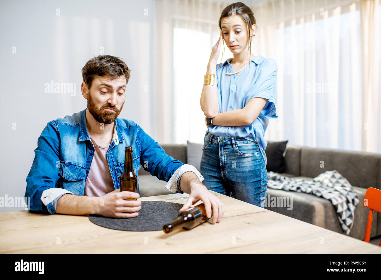 Drunk man suffering from alcoholism feeling depressed sitting at home with young woman in despair on the background Stock Photo