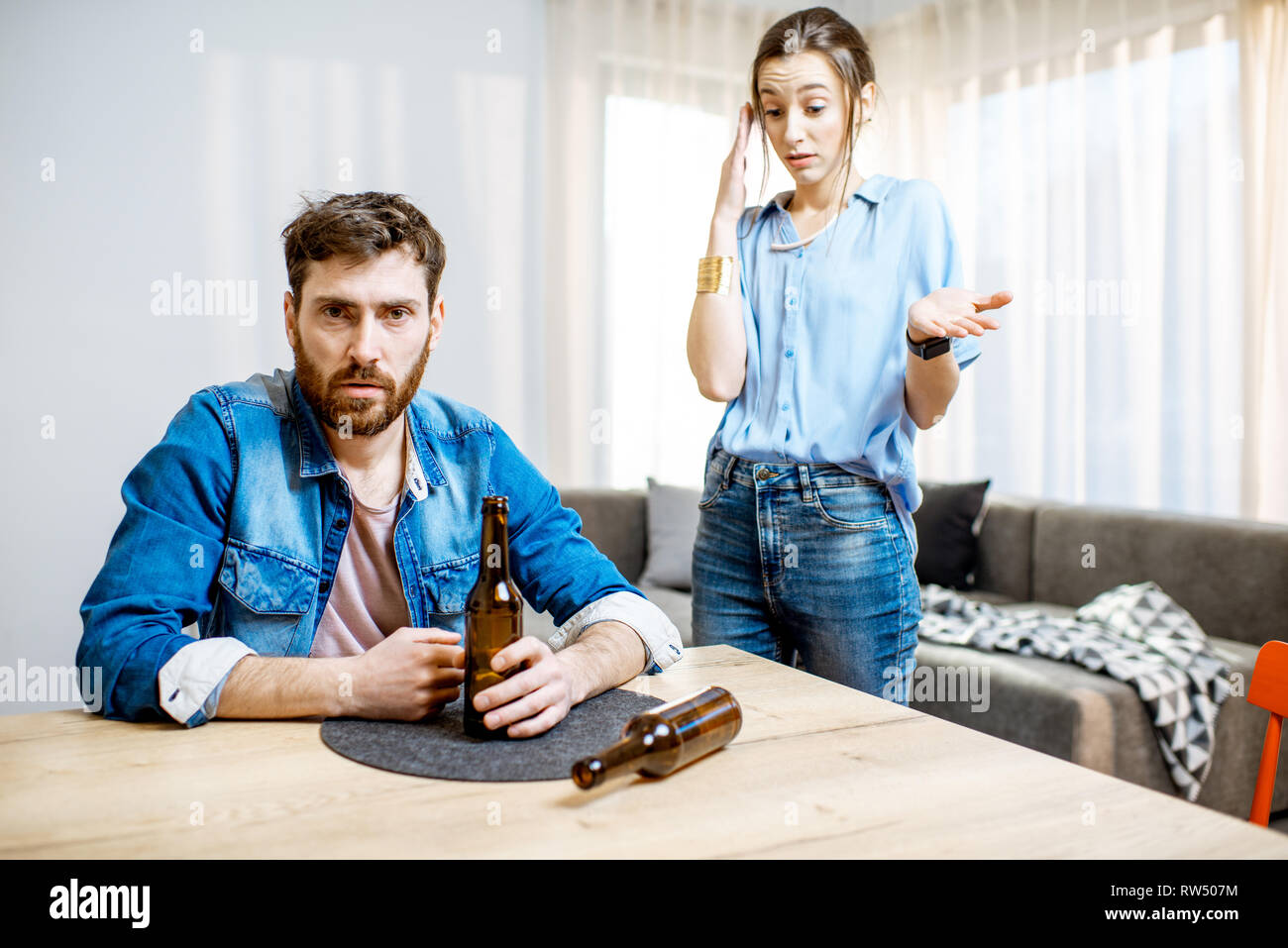 Drunk man suffering from alcoholism feeling depressed sitting at home with young woman in despair on the background Stock Photo