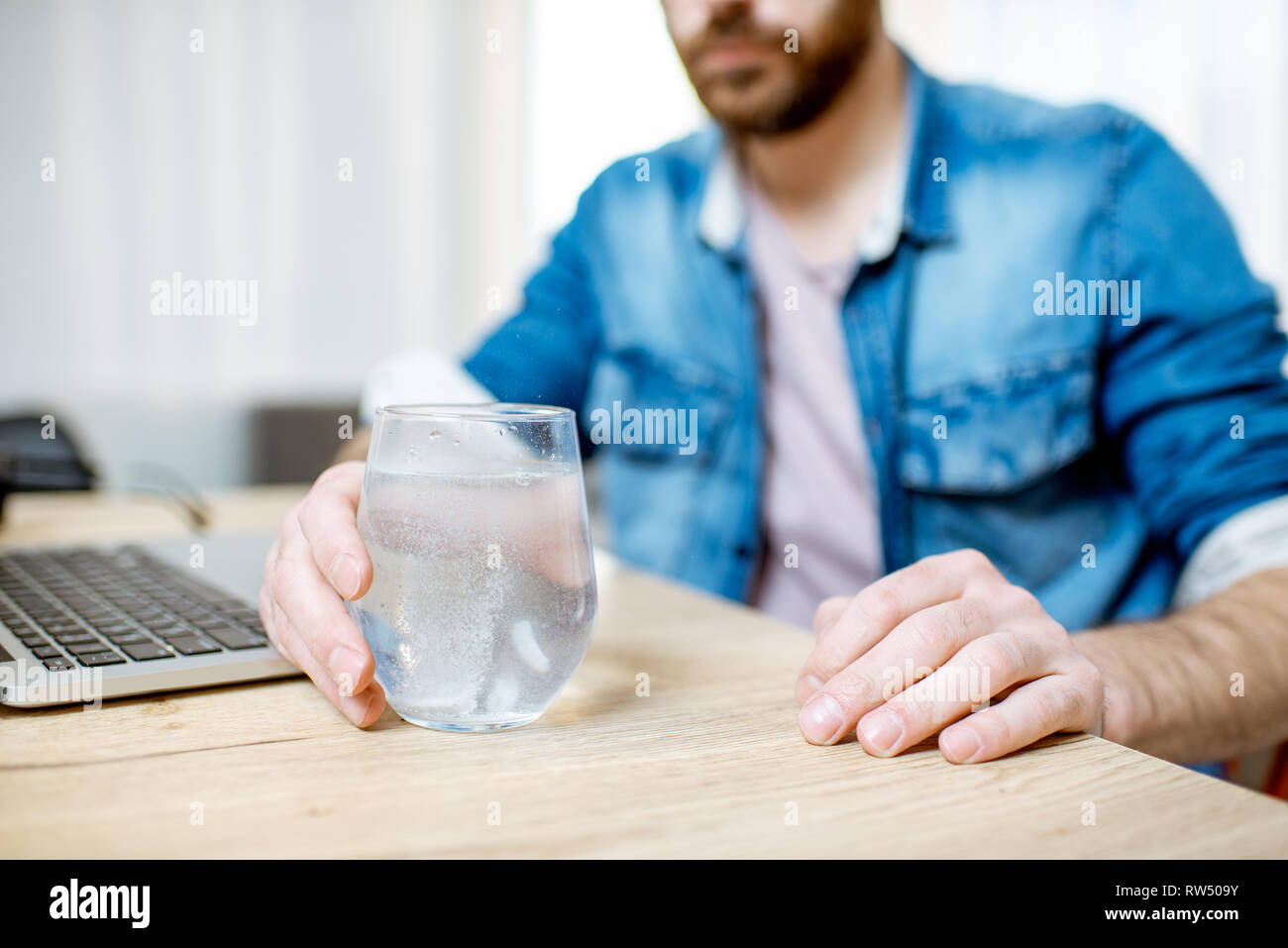 Man taking antipyretic or analgesic pills feeling bad while working on the laptop at home Stock Photo