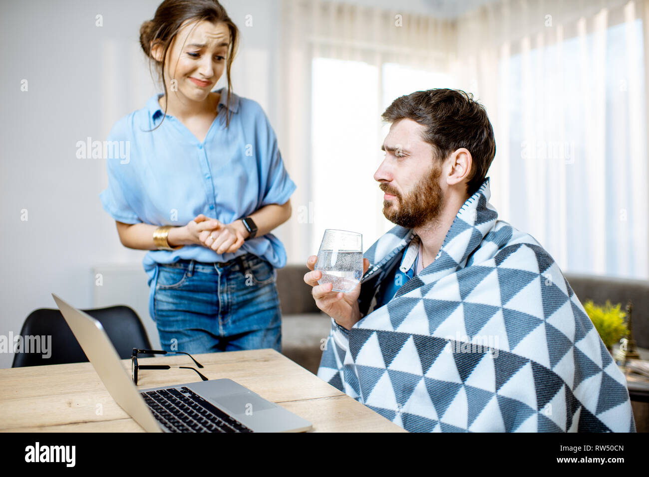 Young woman taking care giving some medicine for a man feeling sick covered with blanket at home Stock Photo