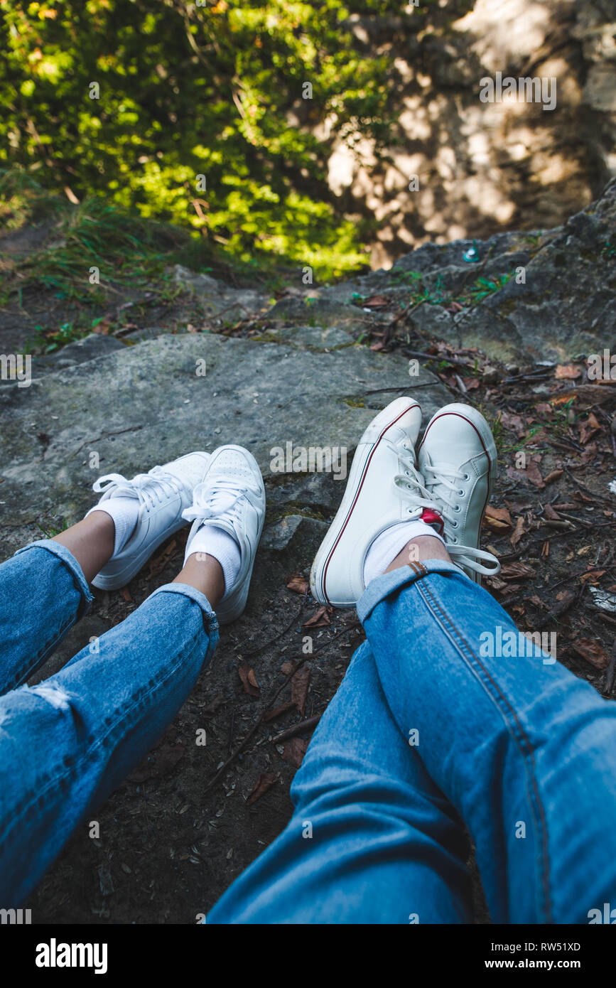 couple sitting on the rocky ground. body parts. legs in white shoes. summer  time Stock Photo - Alamy