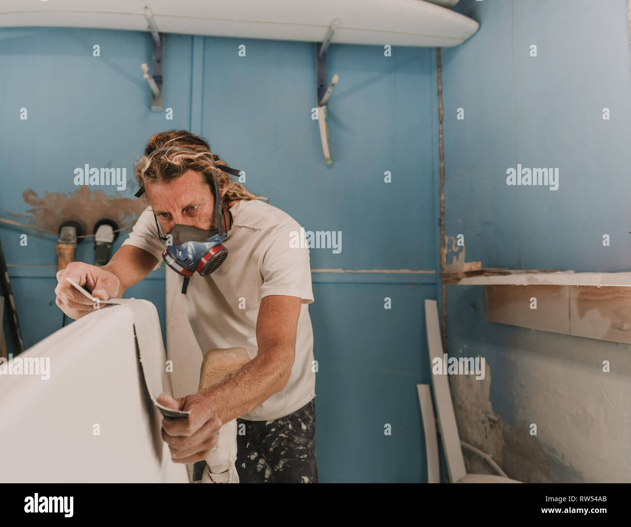 man in respirator measuring surf board in workshop Stock Photo