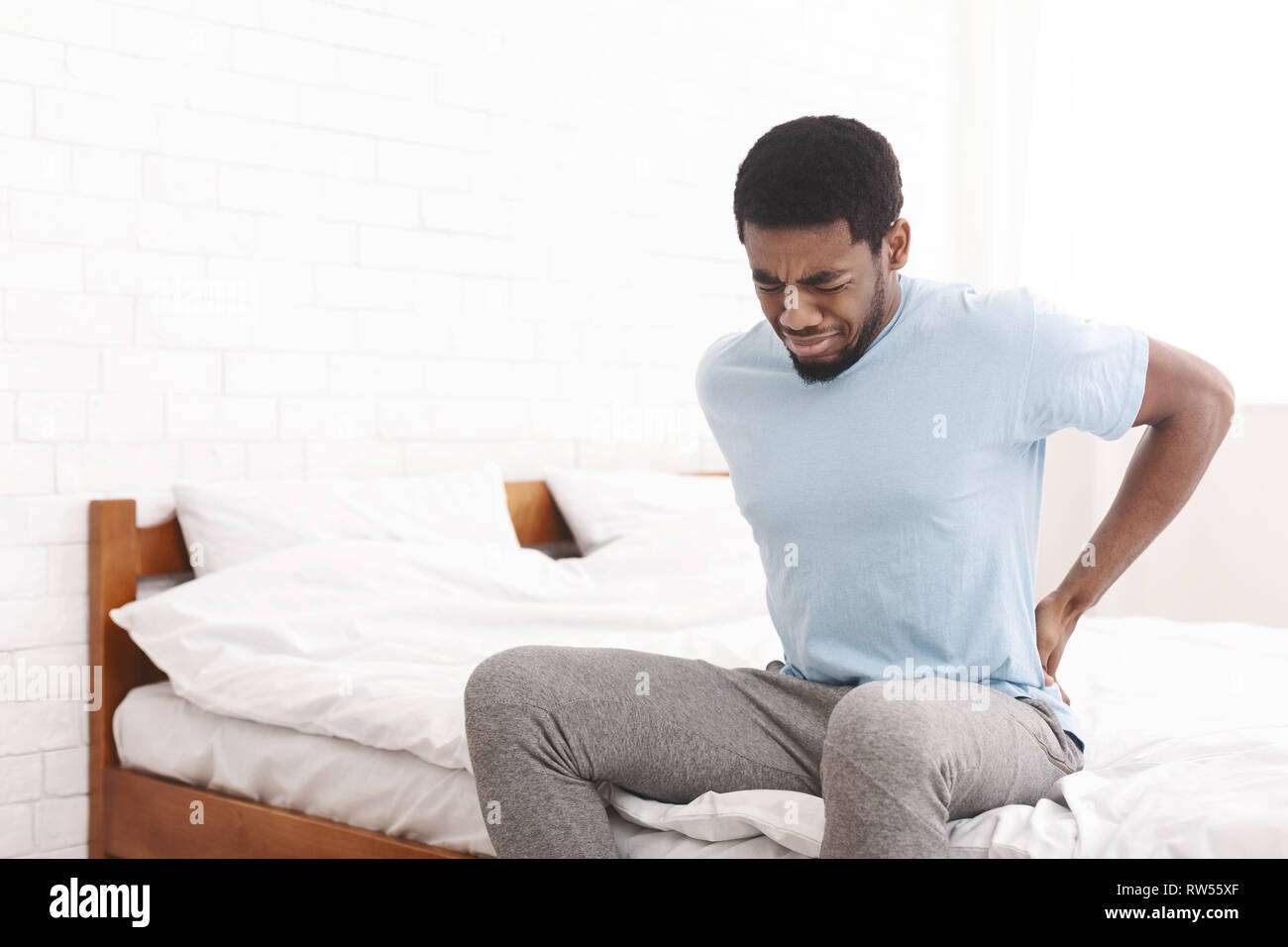 Man suffering from back pain at home in bedroom. Stock Photo