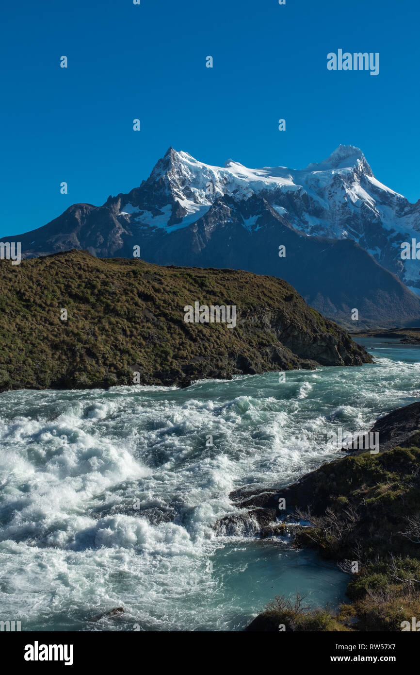 Waterfall cascading with a thunderous roar with a mountain range in the background, Torres del Paine, National Park, Chile, clear blue sky, portrait a Stock Photo