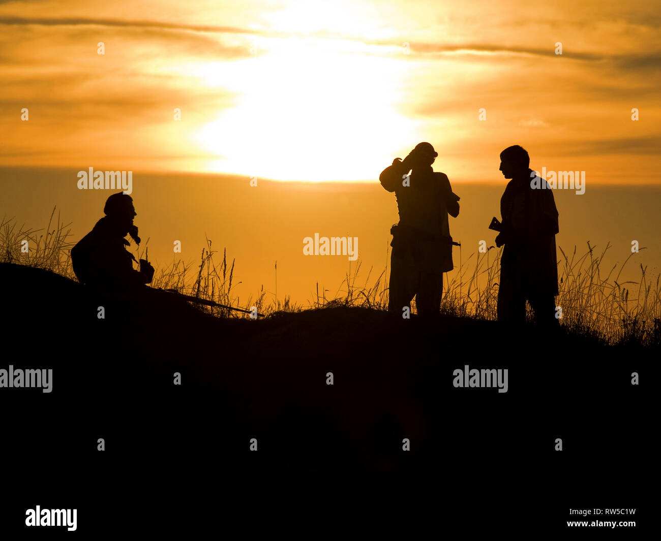 Silhouettes of several soldiers with rifles against a sunset. Stock Photo