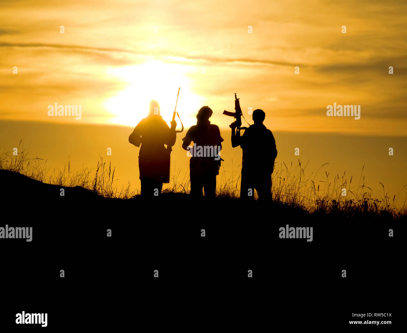 Silhouettes of several soldiers with rifles against a sunset. Stock Photo