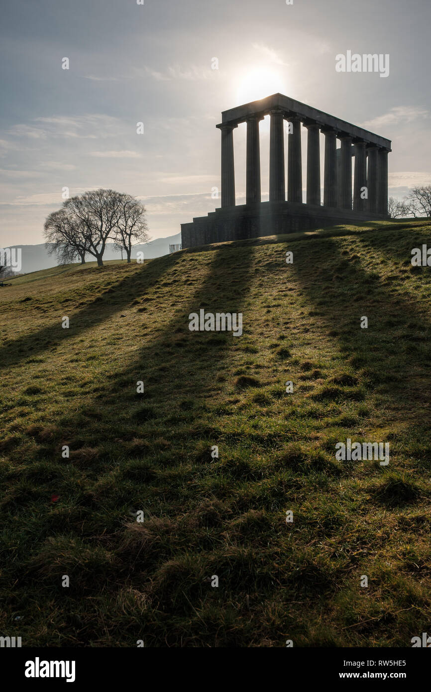 Looking up to the silhouette of the National Monument of Scotland with the sun shining from behind it on Calton Hill in Edinburgh, Scotland Stock Photo