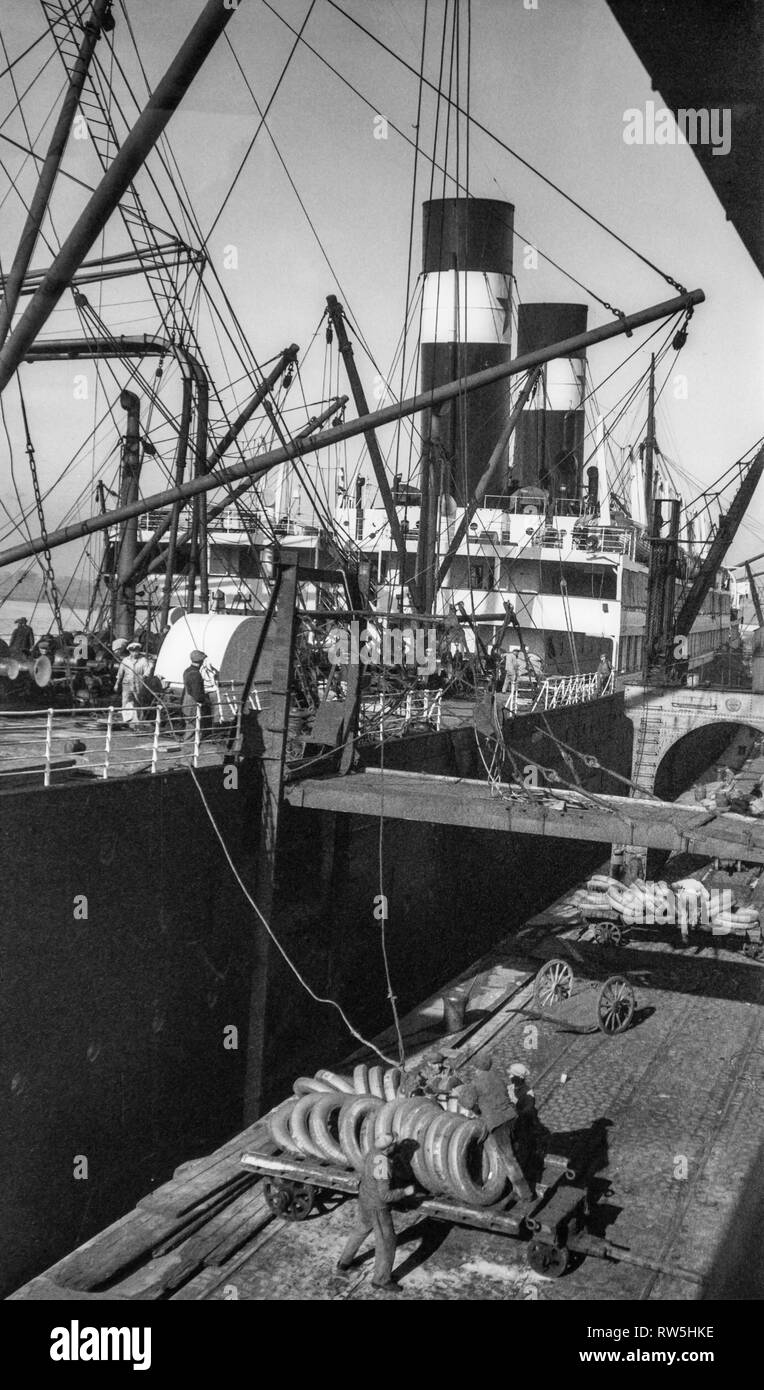 Old early 1900s photo of stevedores / dockers / longshoremen / dockworkers unloading / loading steamship in the port of Antwerp, Belgium Stock Photo