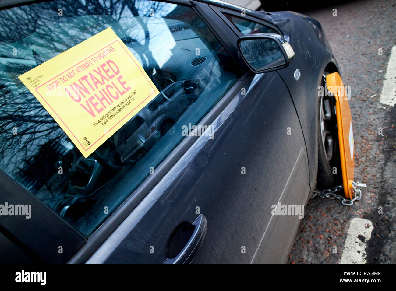 warning label and wheel clamp on untaxed vehicle car clamped on a street in the uk Stock Photo