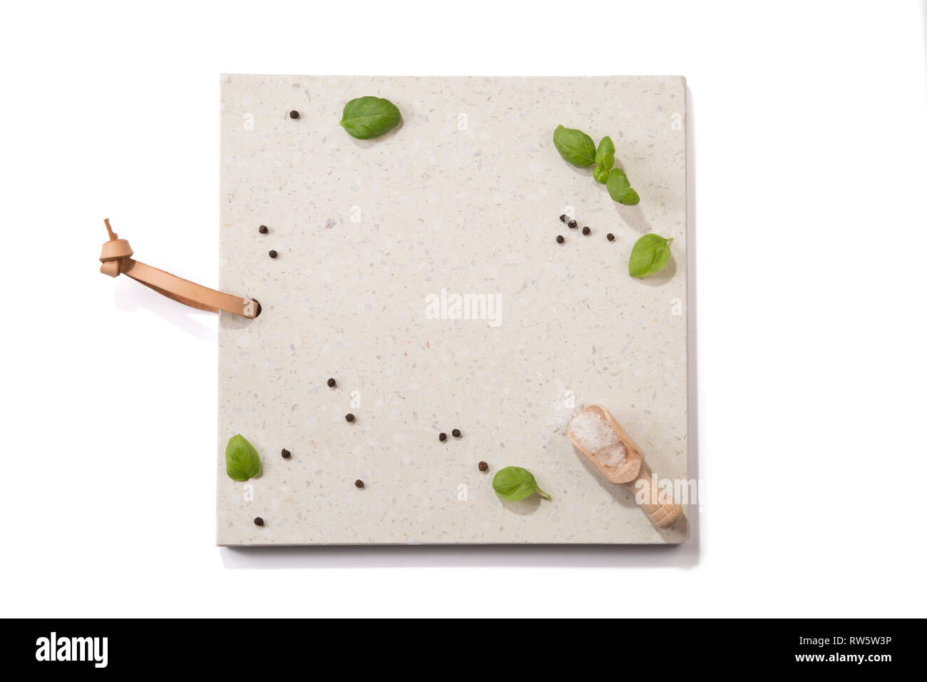 Concrete stone server/board/tray with space for text on white background. Arranged basil leaves, wooden scoop, peppercorns and salt crystals. Top view Stock Photo