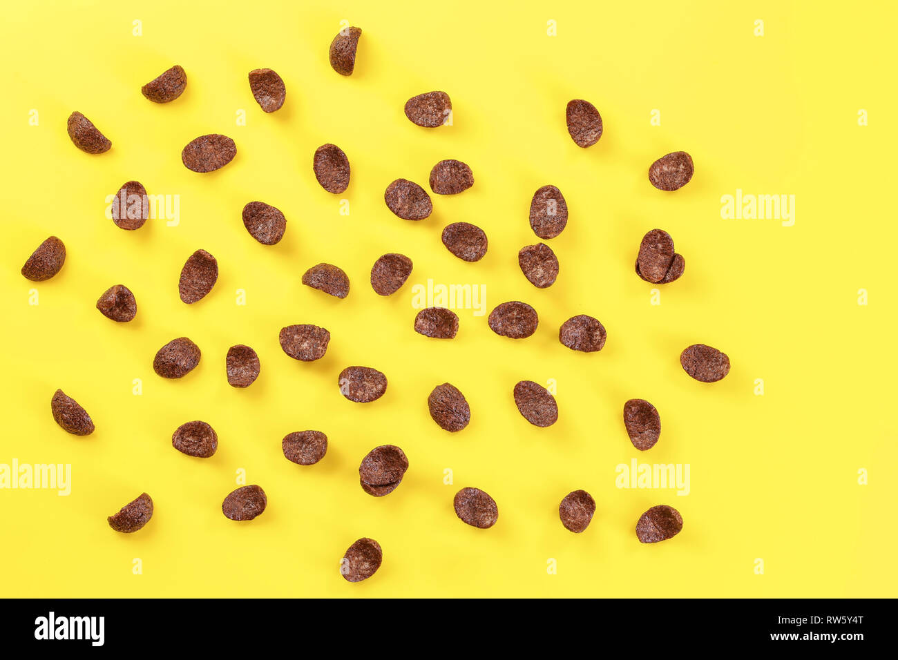 Top down view, chocolate cornflakes scattered on yellow board. Stock Photo
