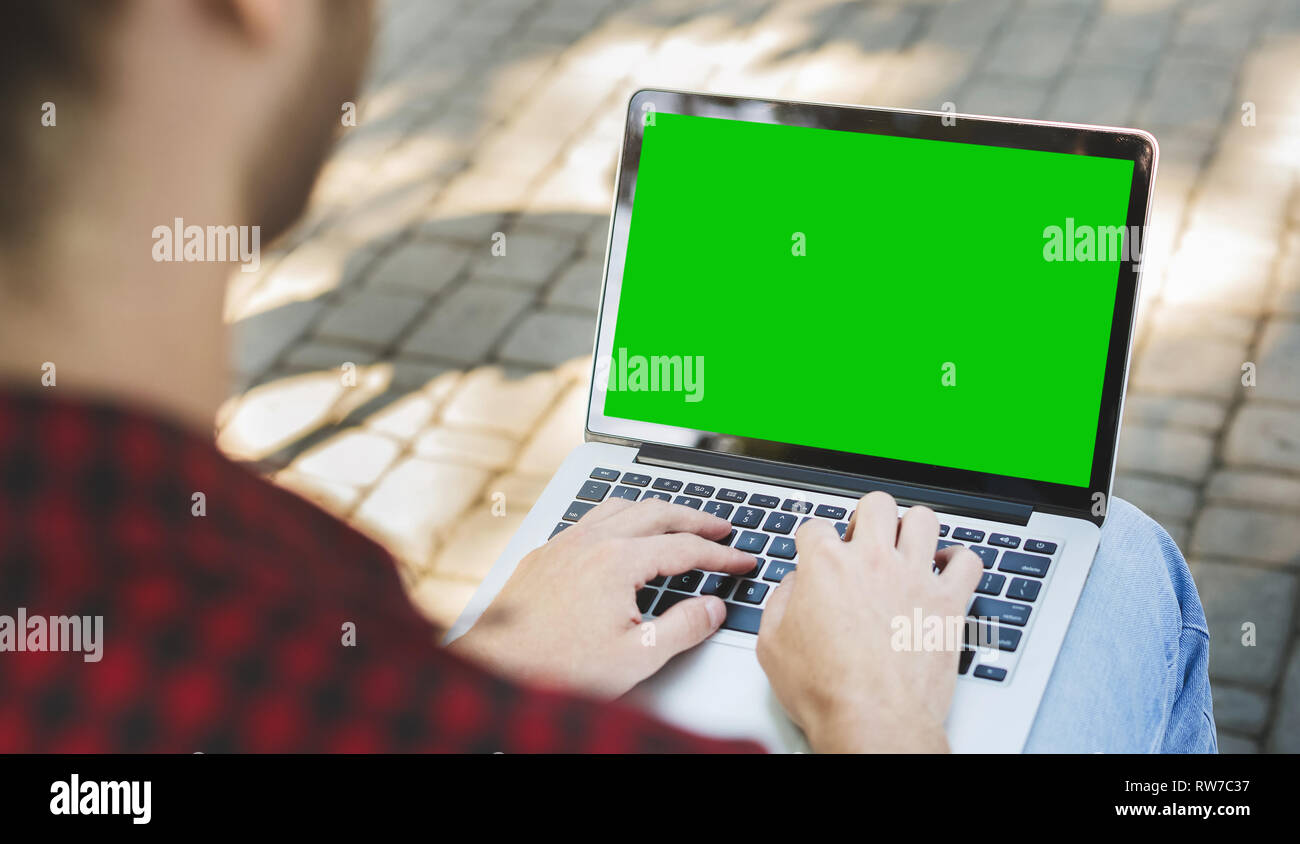 Millennial man typing on laptop with green screen Stock Photo
