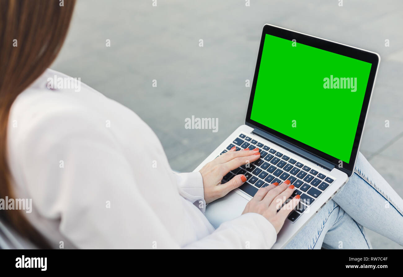 Millennial woman typing on laptop with green screen Stock Photo