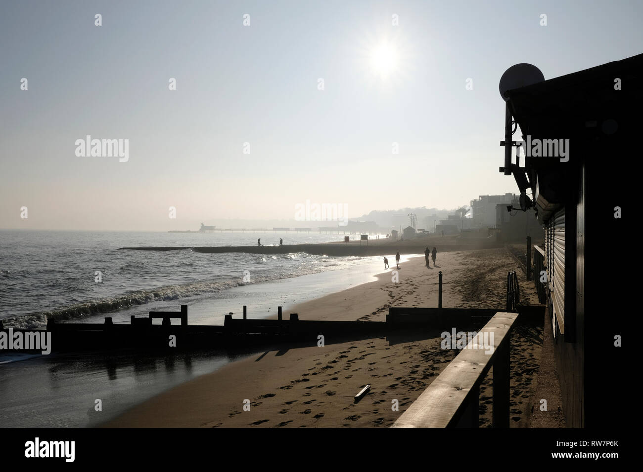 A group of friends walking along Sandown beach in silhouette, in bright hazy sunshine. Stock Photo