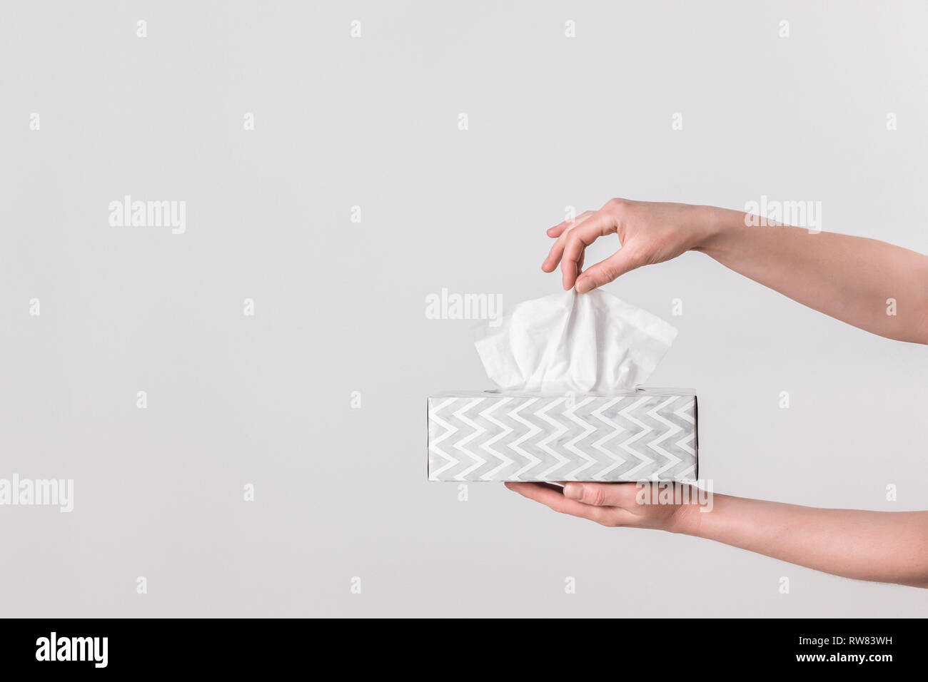 Delicate female hands pulling a tissue out of a gray tissue box. Stock Photo