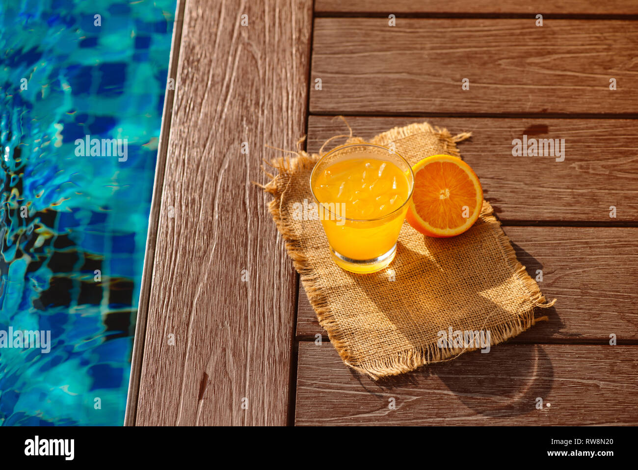 Close up of screwdriver cocktail alcohol drink with orange juice, slices and ice standing near the pool. Refreshing iced lemonade beverage in glass by Stock Photo