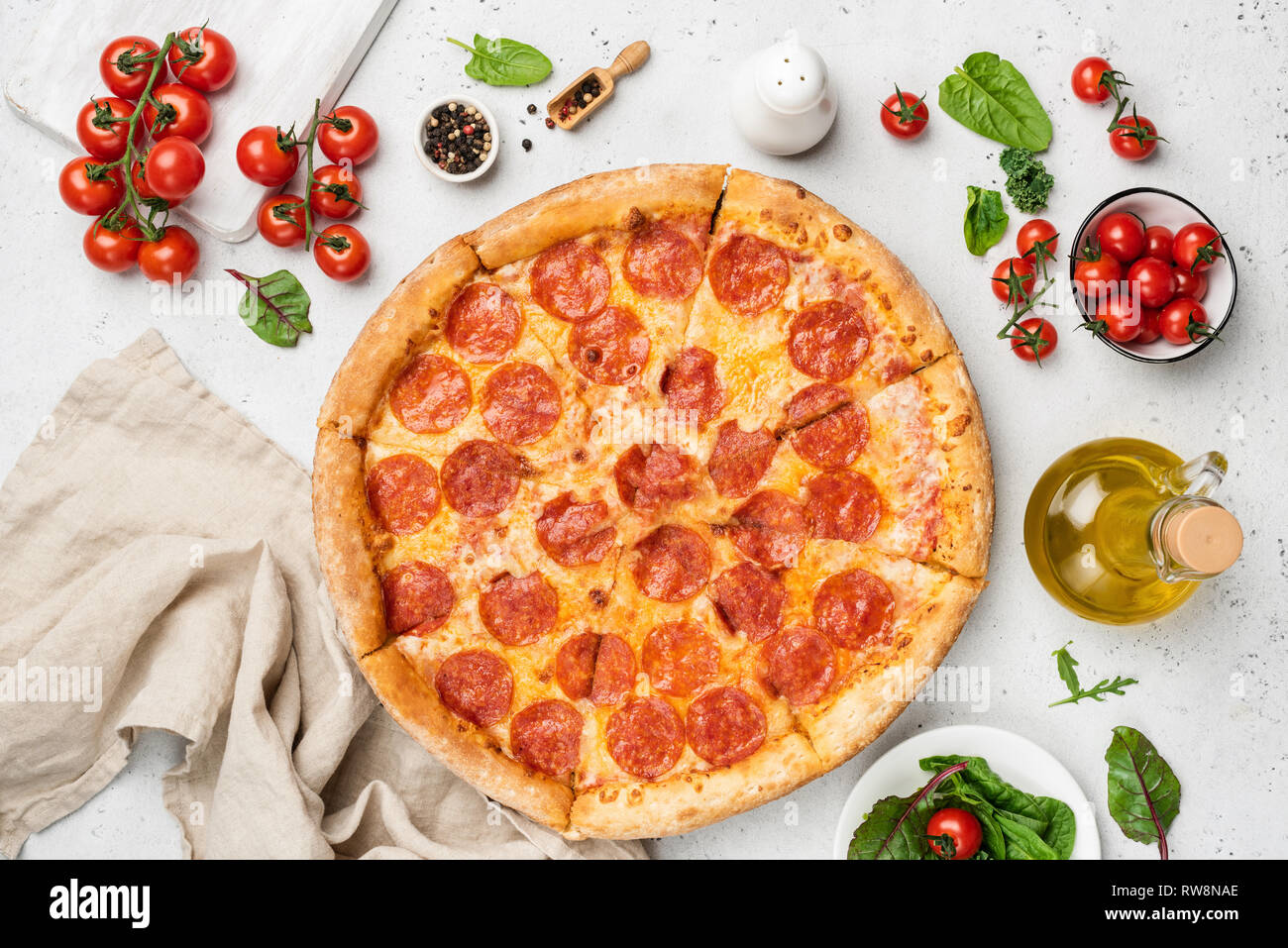 Tasty Pepperoni Pizza On White Background. Pizza, Olive Oil, Cherry tomatoes, Green Leaf Salad Mangold, Arugula and Pepper. Table top view Stock Photo