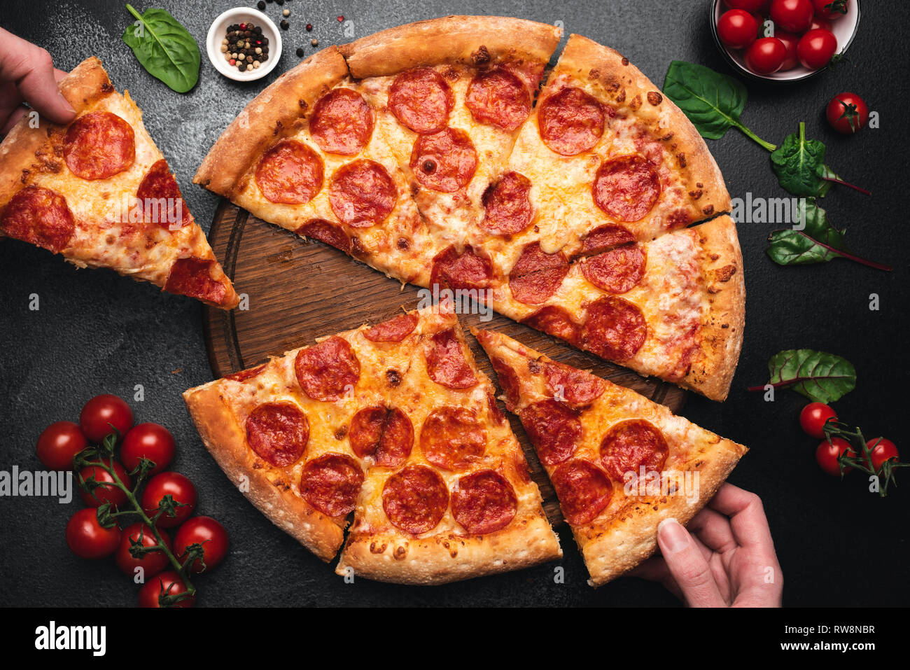 Picking slice of pepperoni pizza. Hands picking pizza slice. Top view of tasty hot pepperoni pizza on black concrete background Stock Photo