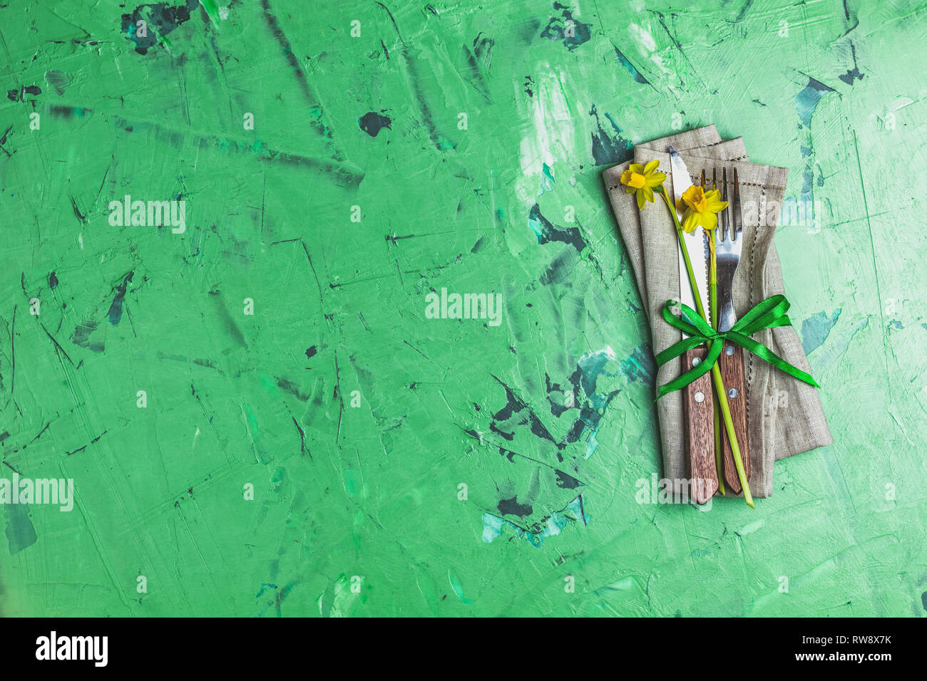 Cutlery with daffodils on a napkin. Top view, green concrete surface background, copy space for you text Stock Photo