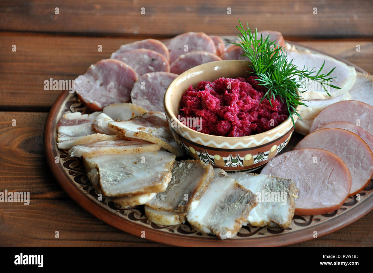 A bowl of grated horseradish with beetroot, served with assortment of lard and sausages